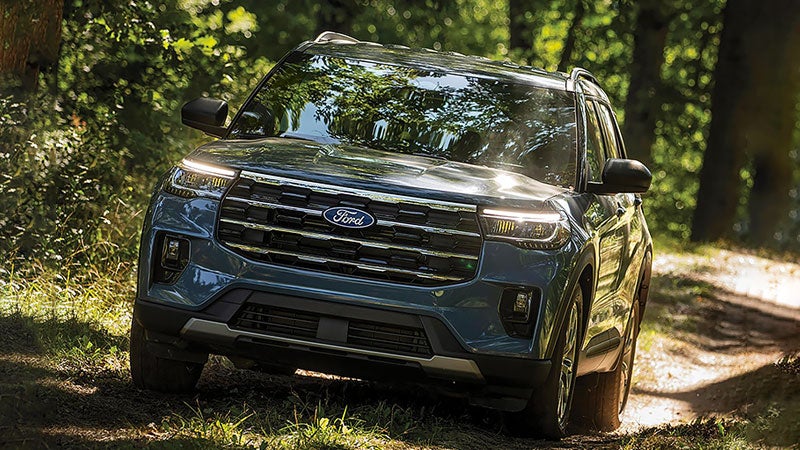 2027 Ford Explorer Active 4WD in Vapor Blue Metallic driving along a wooded mountain trail